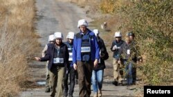 Members of the Organization for Security and Cooperation in Europe (OSCE) Special Monitoring Mission to Ukraine walk along a road as they arrive for monitoring ahead of the proposed withdrawal of troops, in the village of Petrovskoye in Donetsk region, Uk